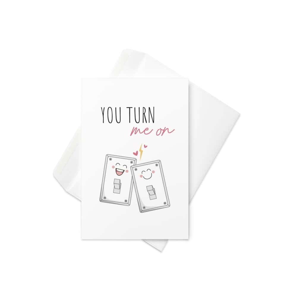 A cute and punny Valentine's Day card featuring two happy light switches with blushing faces and the phrase "You Turn Me On" in a playful font.