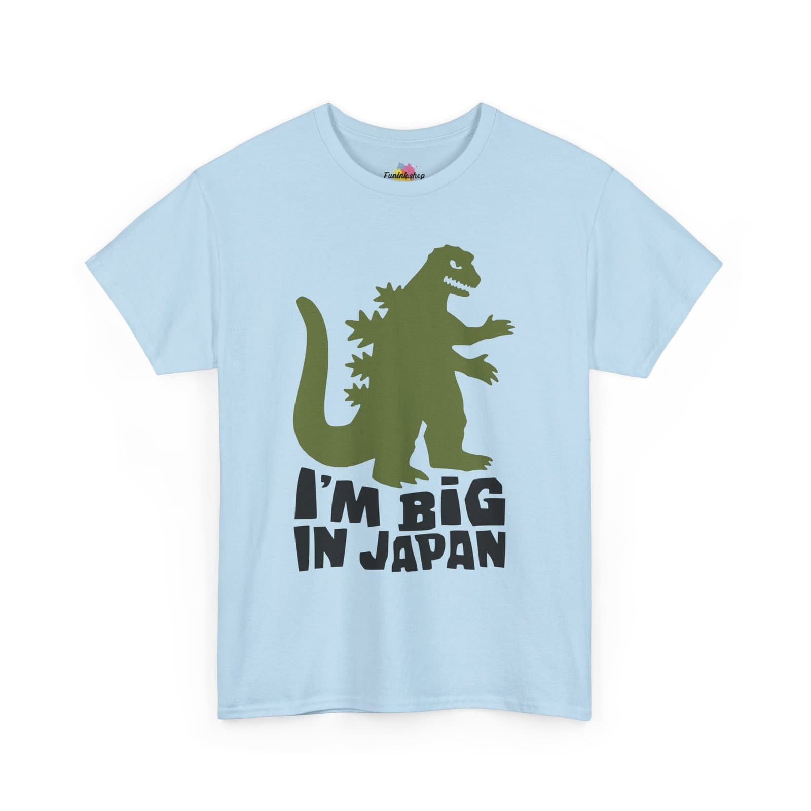A fun and quirky "I'm Big in Japan" t-shirt featuring a green kaiju (Godzilla-style monster) silhouette with bold black text. Available in multiple colors, including light blue, neon green, gray, and white.