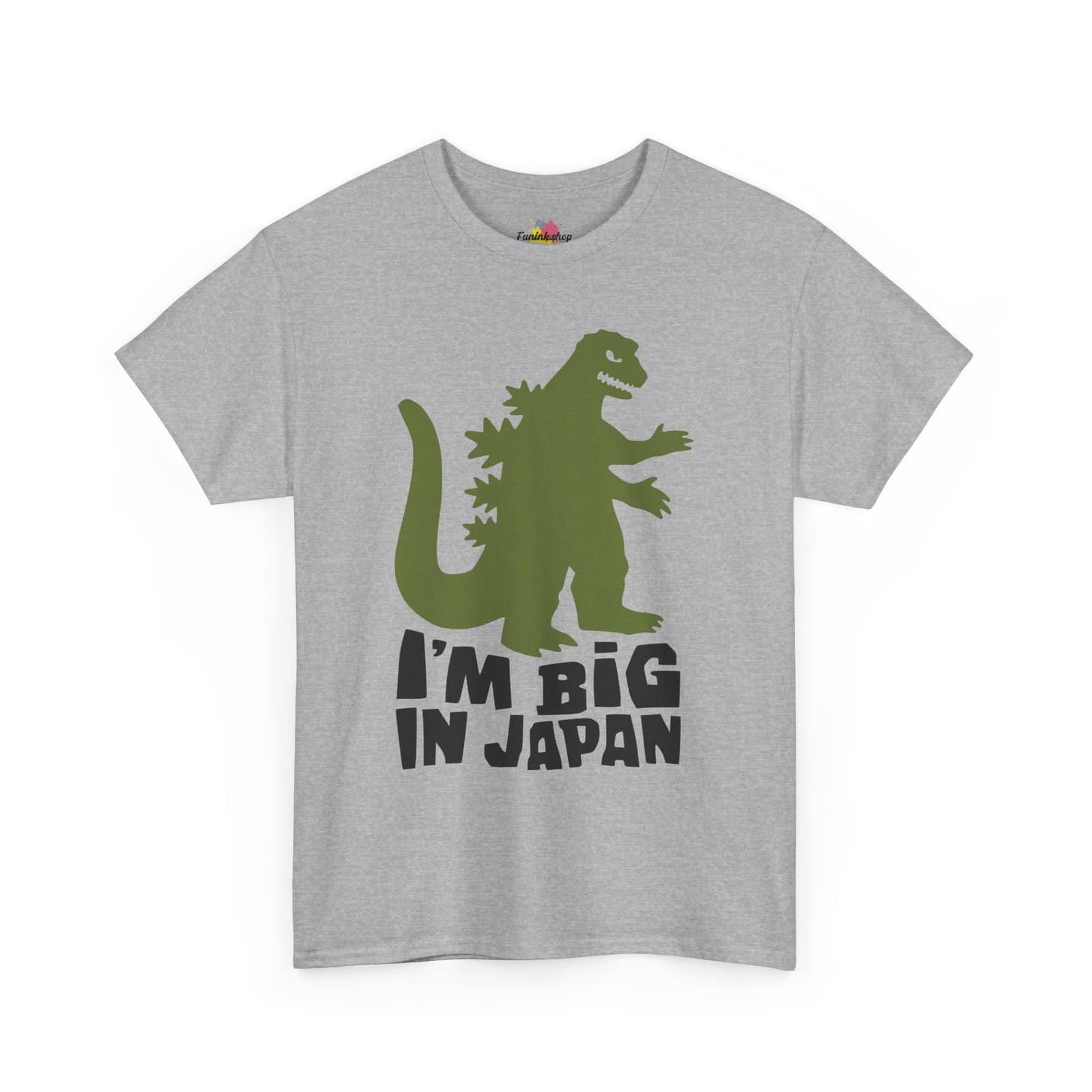 A fun and quirky "I'm Big in Japan" t-shirt featuring a green kaiju (Godzilla-style monster) silhouette with bold black text. Available in multiple colors, including light blue, neon green, gray, and white.